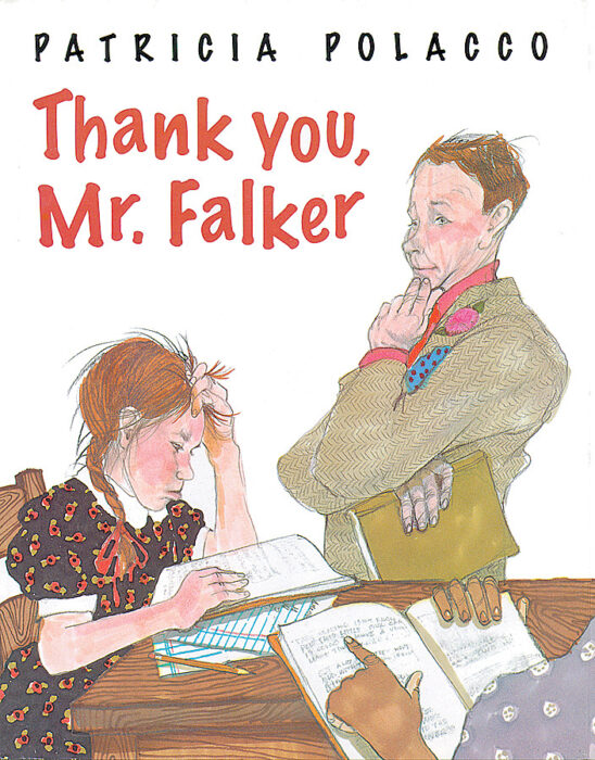 Two students doing work at a desk while a teacher stands over them